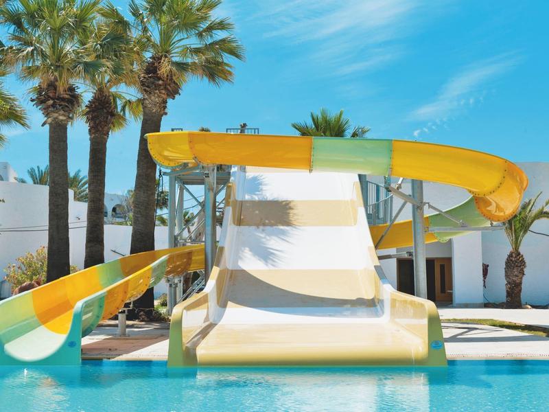 Wasserrutsche in Gelb und Orange über blauem Pool, umgeben von Palmen und hellem Himmel.