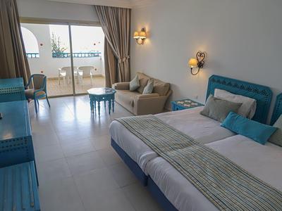 Modern hotel room with double bed, sofa, balcony, and sea view.