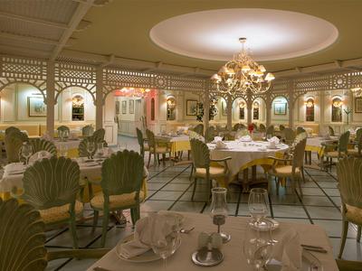 Elegant restaurant with white tablecloths and golden chairs under chandeliers.
