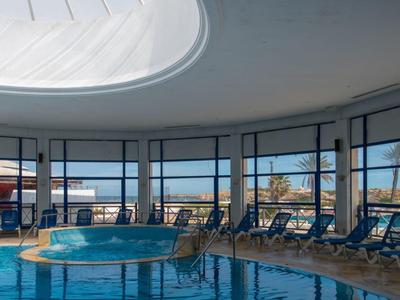 Large indoor pool with panoramic windows and lounge chairs, bright and modern design.