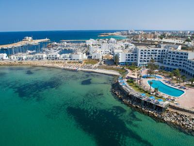 Küstenhotel mit Pool an klarem, blaugrünem Meer und einer Promenade.