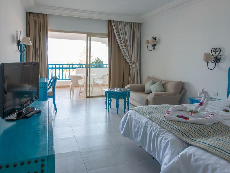 Bright hotel room with terrace and sea view, furnished with bed, armchair, and TV.