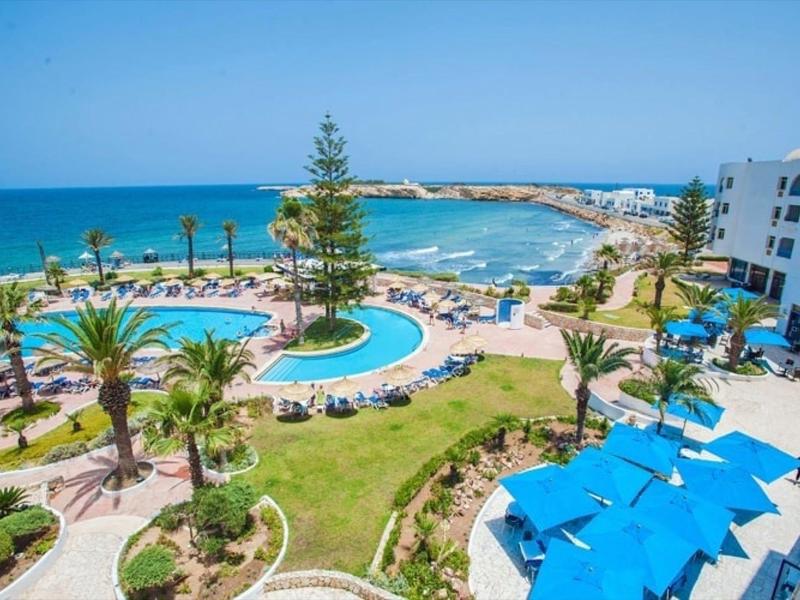 View of a hotel with pool, sun umbrellas, and sea in the background.