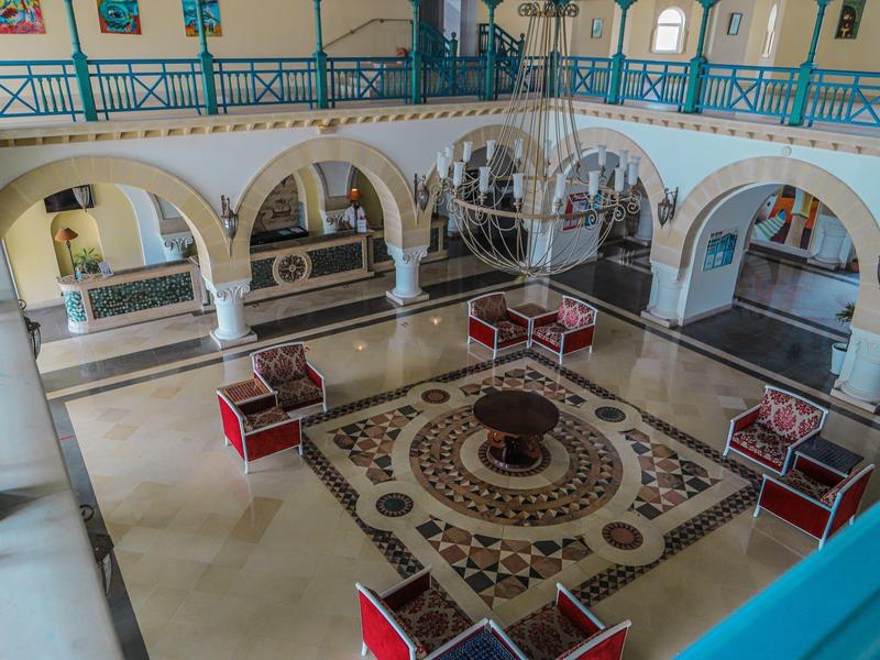 Courtyard of a historic building with patterned floor and seating under arches.