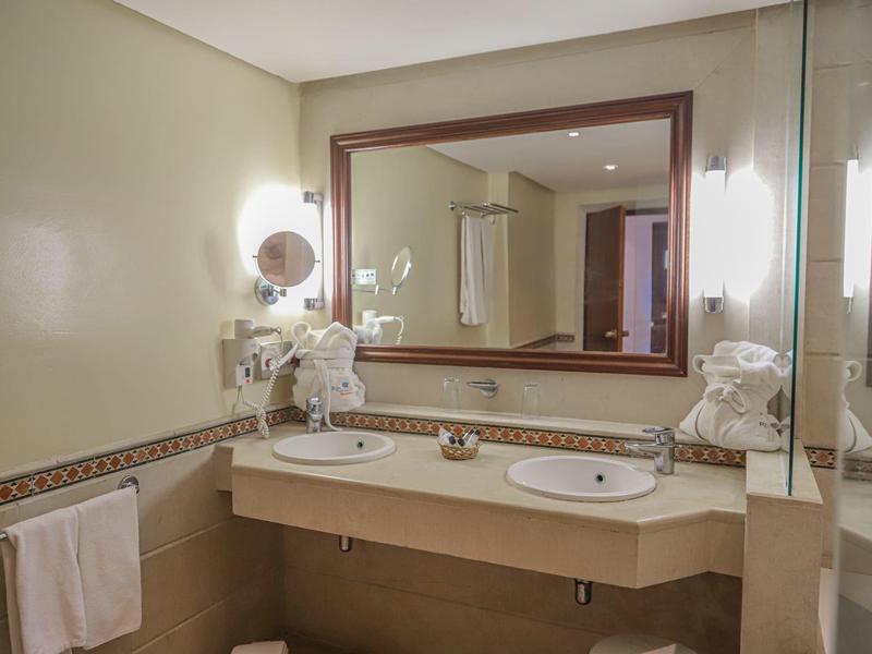 Brightly lit bathroom with two sinks, large mirror, and towels on the wall.