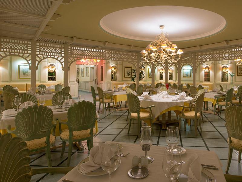 Elegant restaurant with white tablecloths and golden chairs under chandeliers.