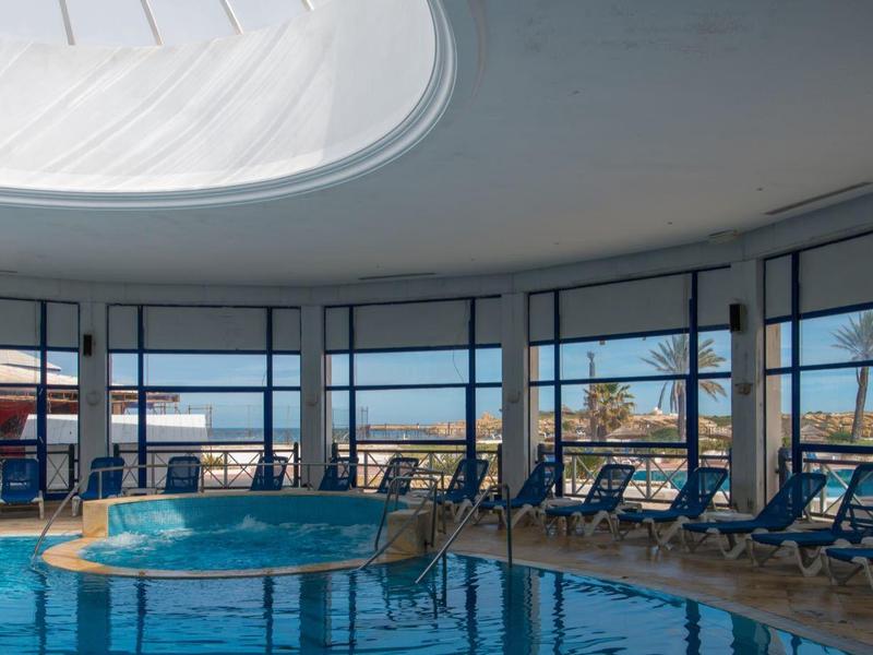 Large indoor pool with panoramic windows and lounge chairs, bright and modern design.