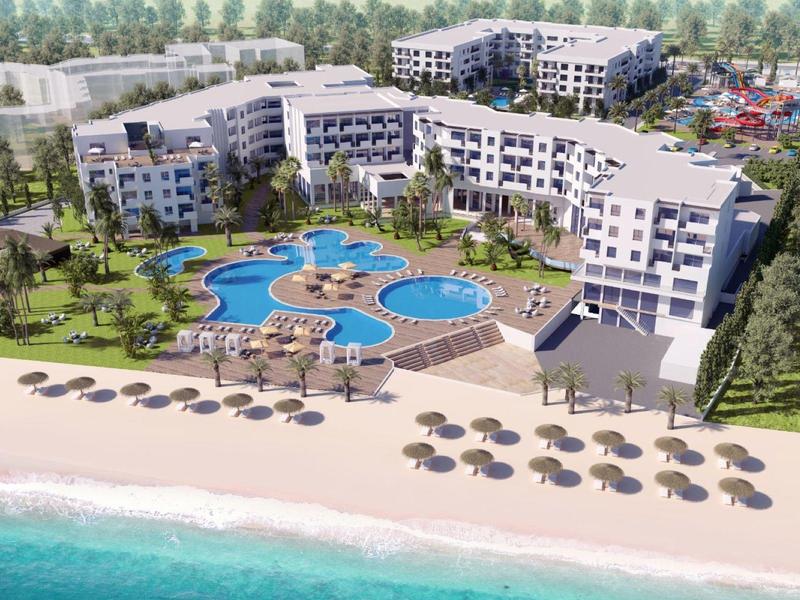 Complesso alberghiero moderno con più piscine, ombrelloni sulla spiaggia e circondato dal verde.