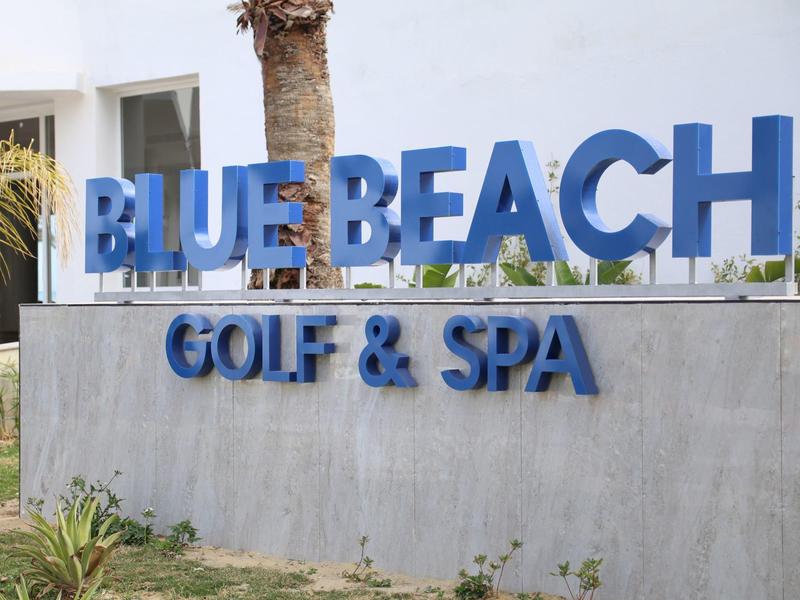 Insegna luminosa blu con la scritta BLUE BEACH GOLF & SPA davanti a un muro.