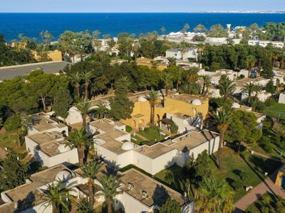 Luftaufnahme eines Wohngebiets mit vielen Palmen, hellen Häusern und blauer Küste im Hintergrund.