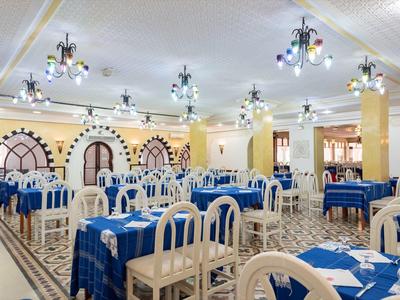 Grande salle à manger avec nappes bleues et chaises blanches, lumineuse et accueillante.