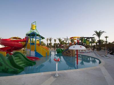 Parc aquatique coloré avec toboggans et champignon d'eau, entouré de palmiers et parasols.