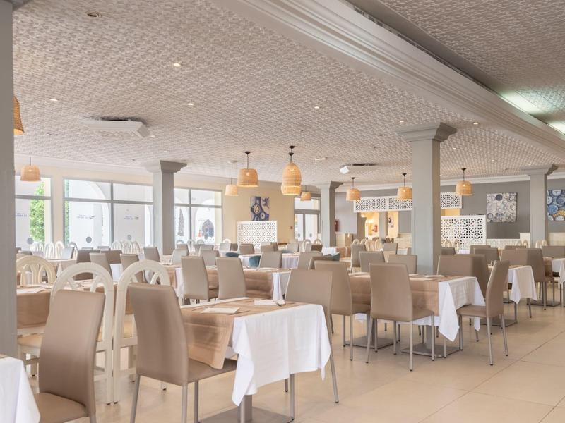 Salle de restaurant moderne avec tables blanches et chaises beiges.