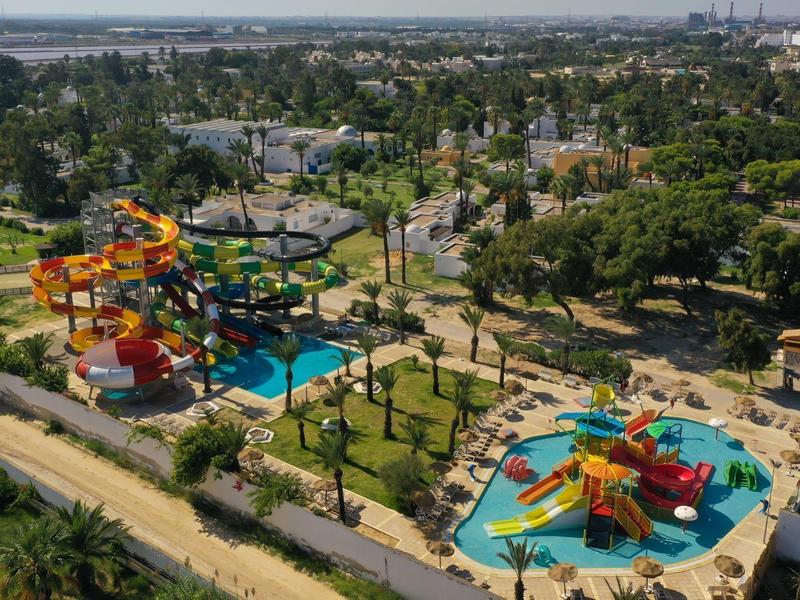 Parc aquatique avec toboggans colorés et piscines entouré d'arbres et de bâtiments en arrière-plan