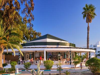 Round hotel restaurant with terrace, palm trees, and clear blue sky in the background.
