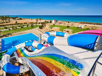 Piscina con tobogán de colores con vista a la playa y al mar bajo un cielo despejado.
