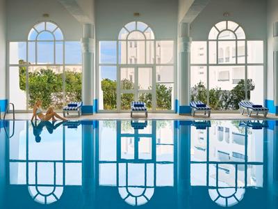 Heated swimming pool with large windows and plants in a bright room.