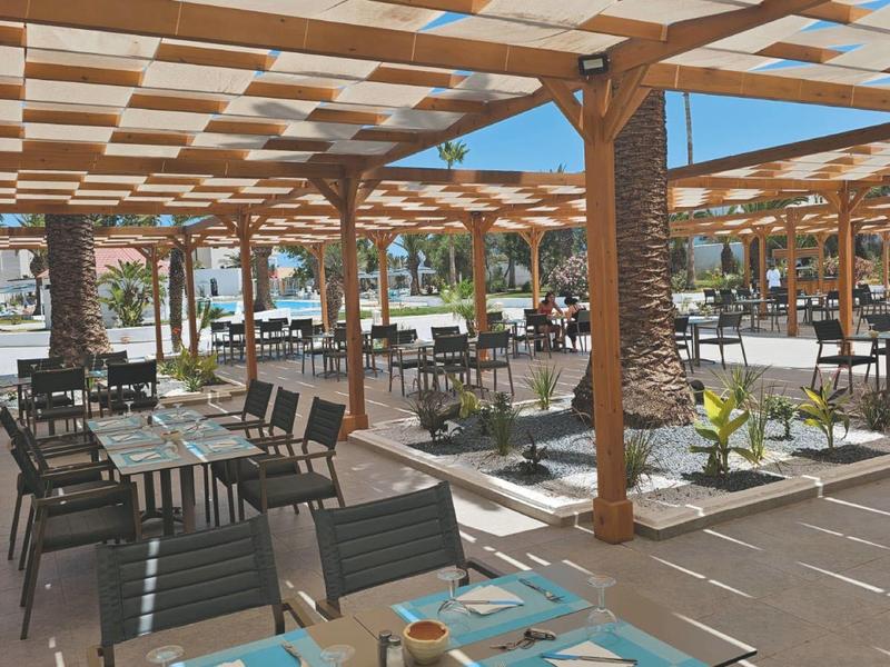 Terraza exterior soleada con techo de madera, mesas y sillas en un restaurante de hotel.