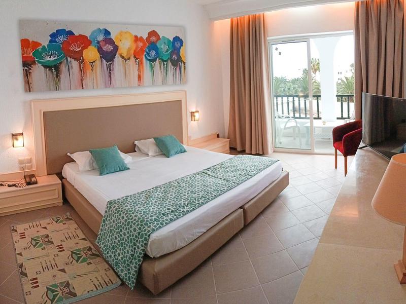 Habitación de hotel moderna con cama doble grande, cuadro colorido y balcón con vista.