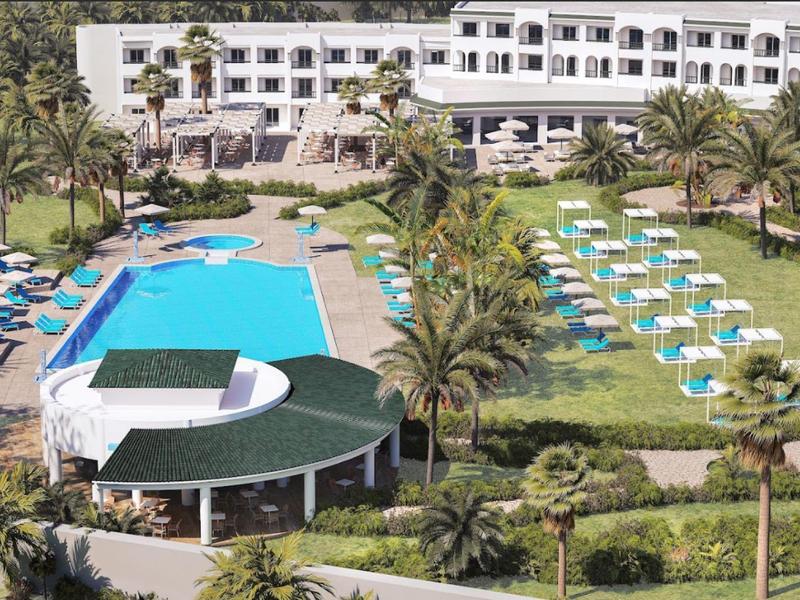 Gran piscina de hotel con tumbonas y sombrillas en un jardín tropical.