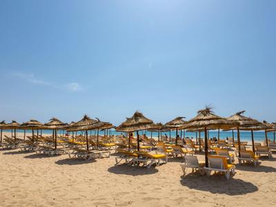 Strand mit Reihen von Strohdächern über Liegestühlen unter blauem Himmel
