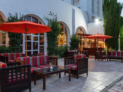 Venkovní část hotelu s posezením pod červenými slunečníky a rostlinami.