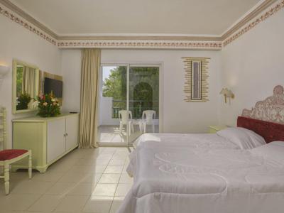 Jasně zařízený hotelový pokoj s manželskou postelí, terasou a výhledem do zahrady.