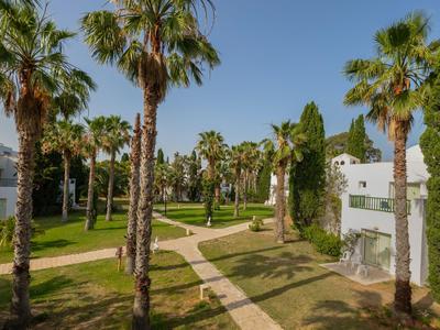 Tuin met palmbomen, gazons en gebouwen onder een heldere hemel bij een hotelresort.