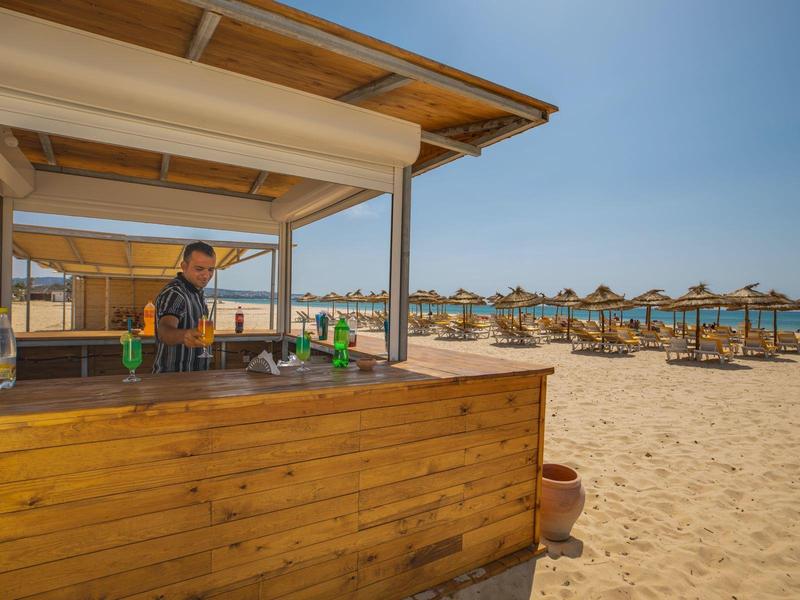 Dřevěný plážový bar s barmanem a lehátky s slunečníky na písku