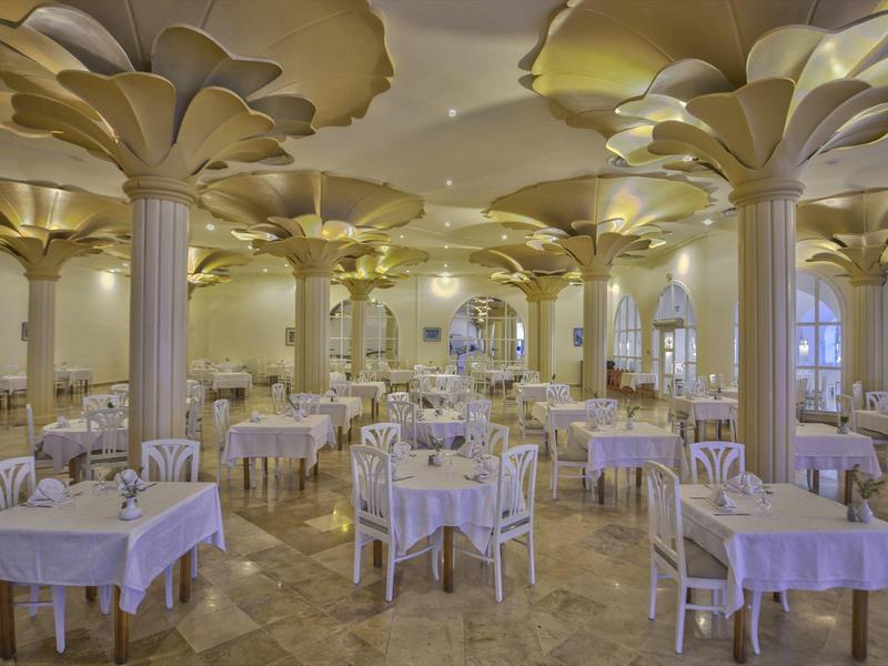 Elegantní jídelna s bílými ubrusy a zlatými zdobenými sloupy v hotelu.