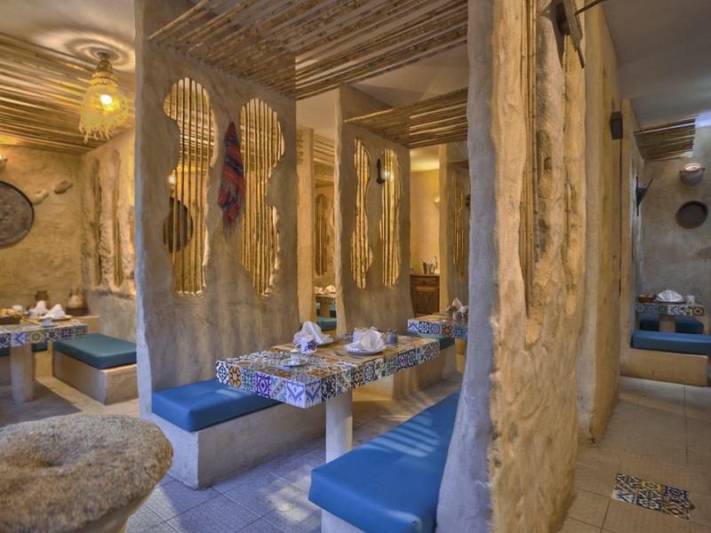 Rustikální restaurace s dřevěnými stěnami a modrými lavicemi, stoly prostřené nádobím.