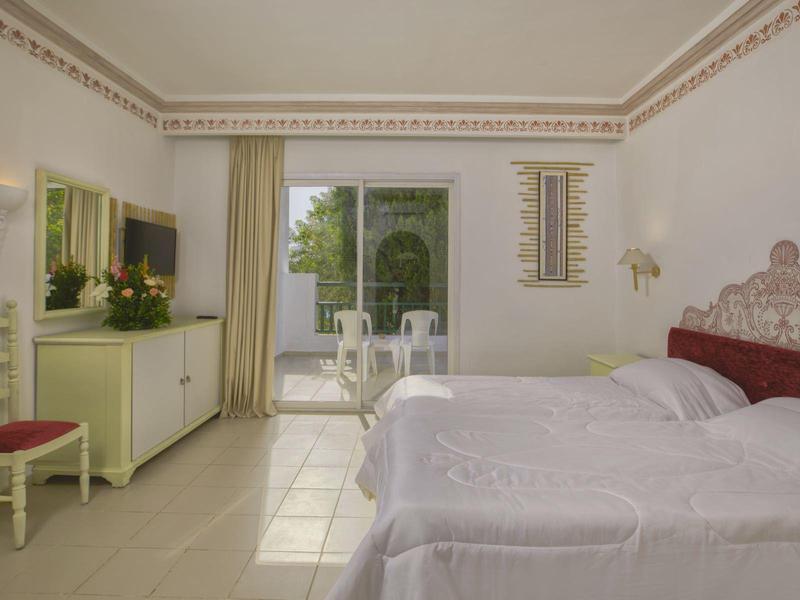 Jasně zařízený hotelový pokoj s manželskou postelí, terasou a výhledem do zahrady.