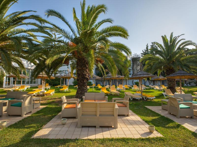 Hotelová zahrada s palmami, posezením a lehátky za slunečného počasí