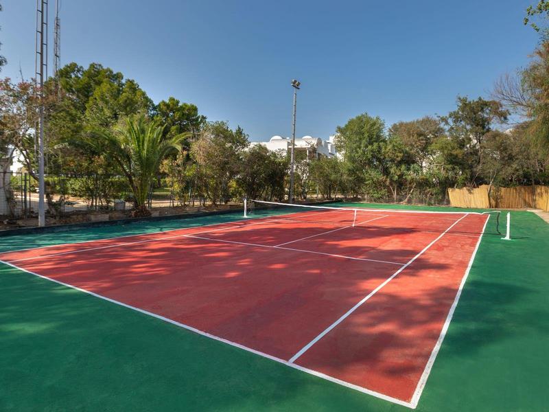 Prázdný venkovní tenisový kurt s červeno-zeleným povrchem pod modrou oblohou