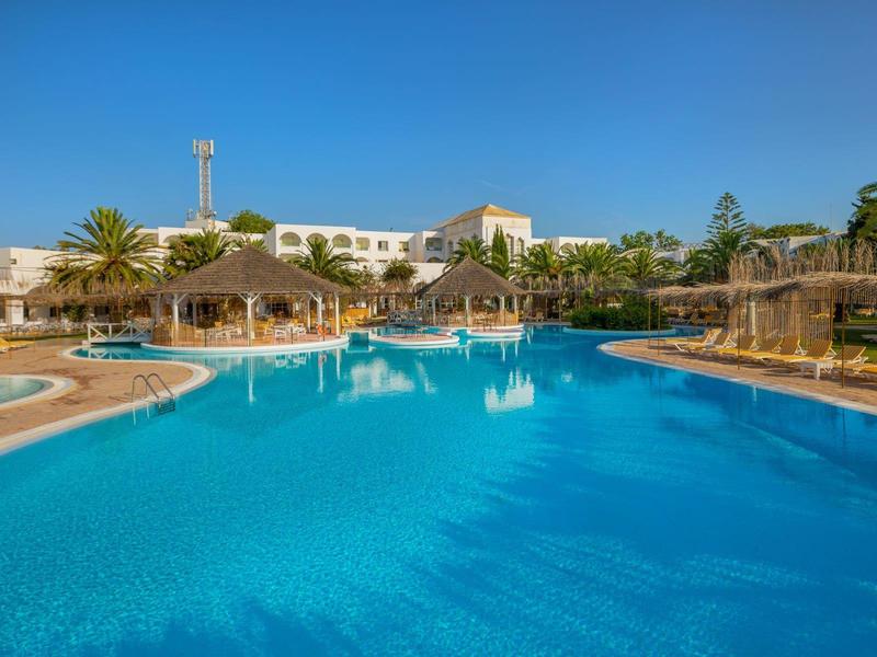 Velký hotelový bazén s slunečníky a lehátky pod modrou oblohou