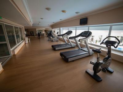 Interieur van een moderne sportschool met loopbanden en hometrainers, grote ramen en houten vloer.