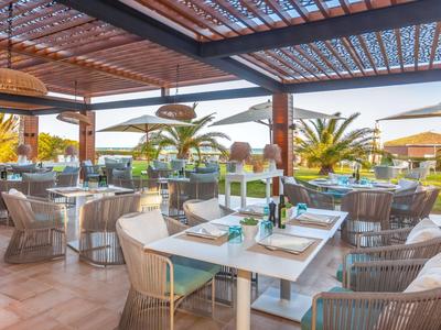 Lichte buitenterras met gedekte tafels en tropische planten in de hoteltuin.