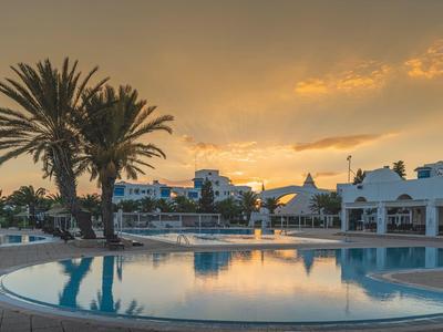 Runder Swimmingpool mit Palmen und weißer Hotelanlage bei Sonnenuntergang.