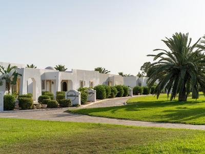 Witte bungalows met groene gazons en palmbomen onder een heldere lucht.