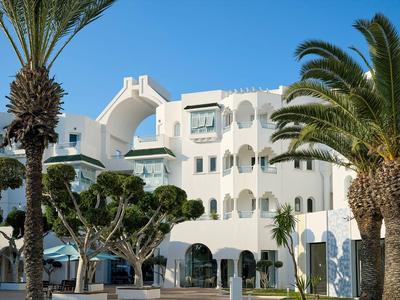 Wit hotelgebouw in mediterrane stijl met palmbomen en heldere blauwe lucht.