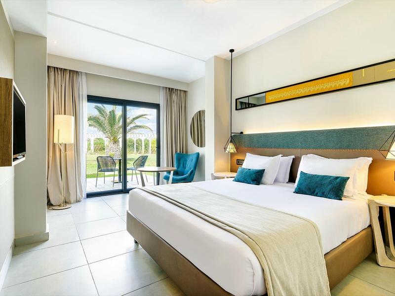 Habitación de hotel moderna con cama doble, balcón y vista al mar en ambiente luminoso.