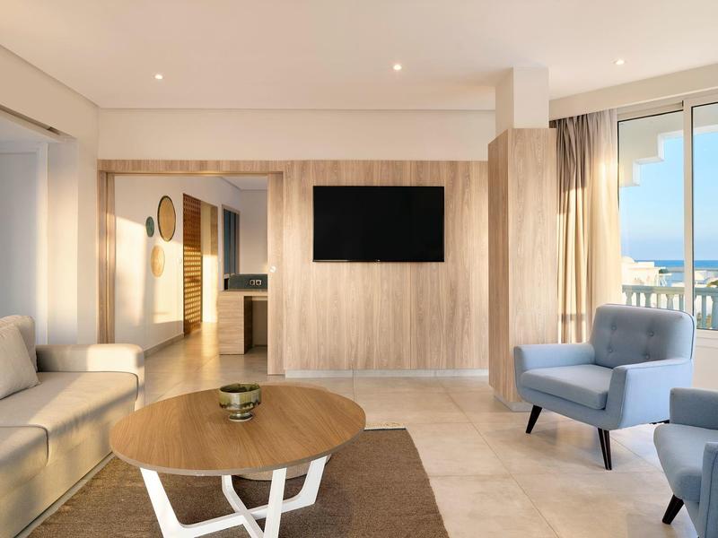 Habitación de hotel moderna con sofá, sillones y vista al mar a través de grandes ventanas.