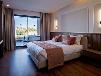 Modernes Schlafzimmer mit großem Fenster, Doppelbett, Holzboden und warmen, erdigen Farbtönen.