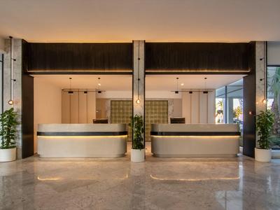 Moderne Hotellobby mit zwei hellen Empfangstheken, Pflanzen und poliertem Steinboden.