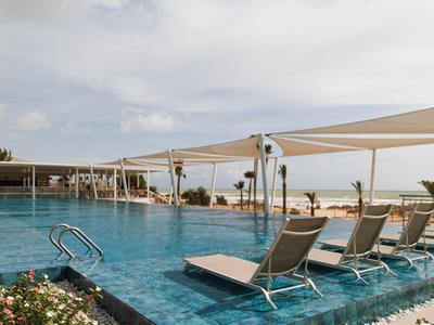 Piscina esterna moderna con lettini e tende da sole con vista sul mare.