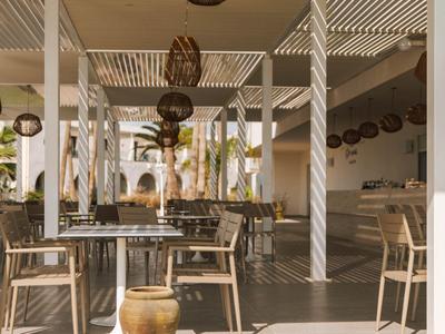 Hell eingerichtetes, offenes Restaurant mit Holztischen und Stühlen unter einer Pergola.