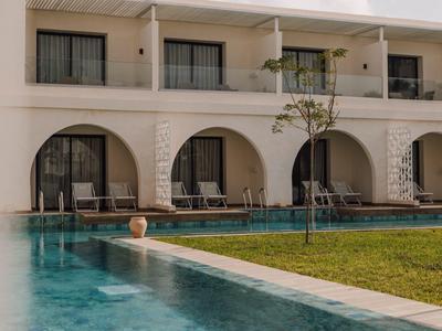 Piscina moderna del hotel con tumbonas frente a habitaciones con grandes ventanas de arco y área verde.