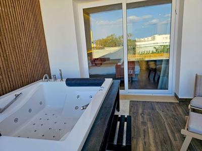 Bañera de hidromasaje en terraza con pared de madera y vista a través de puerta corredera de vidrio al exterior.