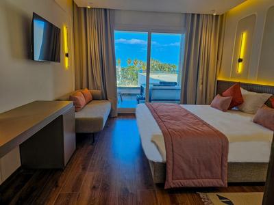 Habitación de hotel moderna con cama, sofá y balcón con vistas al mar a la luz del día.