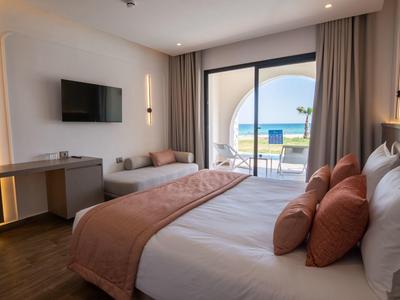Helles Hotelzimmer mit Doppelbett, Balkon und Meerblick, modernen Möbeln und warmen Farben.